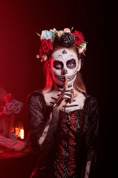 Przerażająca dama śmierci robi cichy znak, aby zachować tajemnicę, ubrana w kostium na halloween santa muerte i pokazująca wyciszony i tajemniczy gest palcem na ustach, święty dios de los muertos.