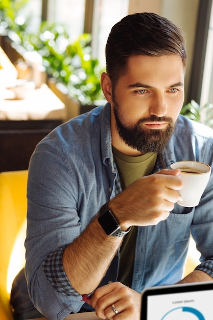 Przerwa na kawę. Poważny brodaty mężczyzna siedzący z filiżanką kawy podczas przerwy na kawę