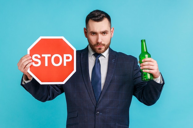 Zdjęcie przestań pić alkohol nie jedź pijany niespokojny biznesmen pokazując butelkę piwa napojów alkoholowych i znak stop ostrzeżenie i martwiąc się kryty studio strzał na białym tle na niebieskim tle