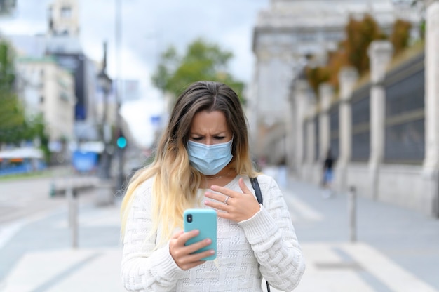 Przestraszona dziewczyna z maską czytająca wiadomości na swoim telefonie na temat choroby ulicznej