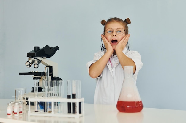 Przestraszona dziewczynka w płaszczu grająca naukowca w laboratorium za pomocą sprzętu
