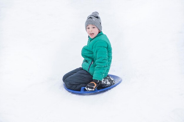 Przestraszony chłopiec zjeżdża ze wzgórza na spodek śniegu Koncepcja sezonowa Zimowy dzień