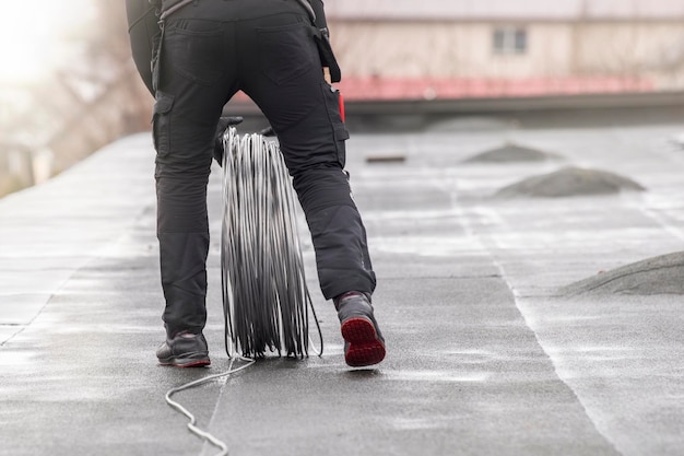 Przewód uziemiający pracownik kładzie kabel uziemiający na dachu elektryka budowlanego mocującego drut aluminiowy