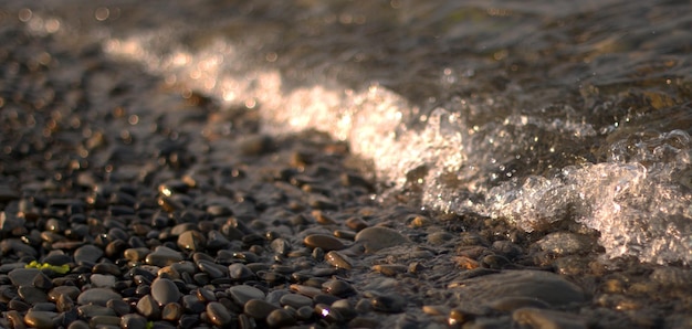 Przezroczysta fala morska toczy się po kamienistej plaży, rekreacja i podróże, rozmycie, bokeh.