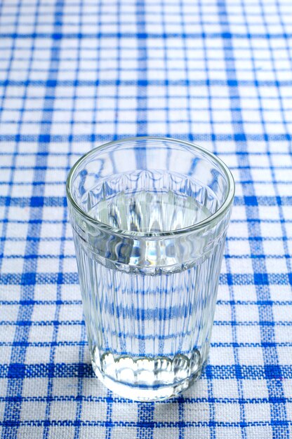 Przezroczysta fasetowana szklanka wody na niebieskim obrusie