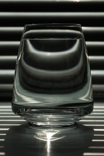 Przezroczysty szklany kubek z czystą wodą na tle ekranu w paski z promieniami światła Układ szablonu tekstura tła makro dyfuzja czarno-biały pionowy