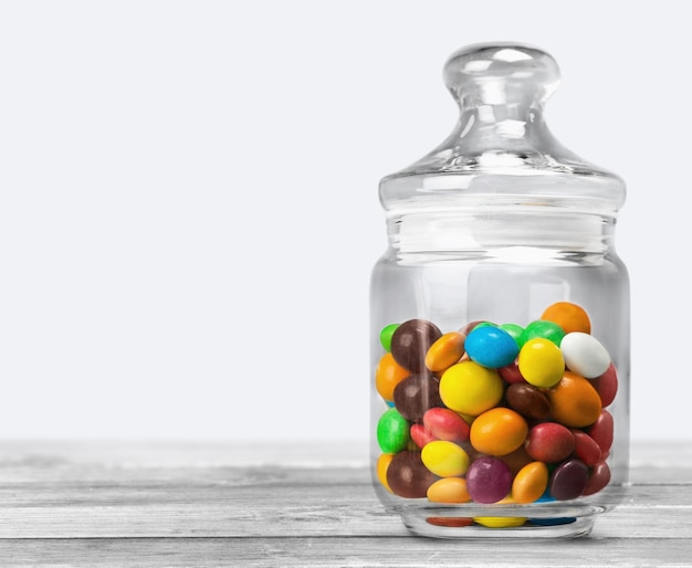 Przezroczysty szklany słoik z kolorowymi czekoladowymi cukierkami na stole