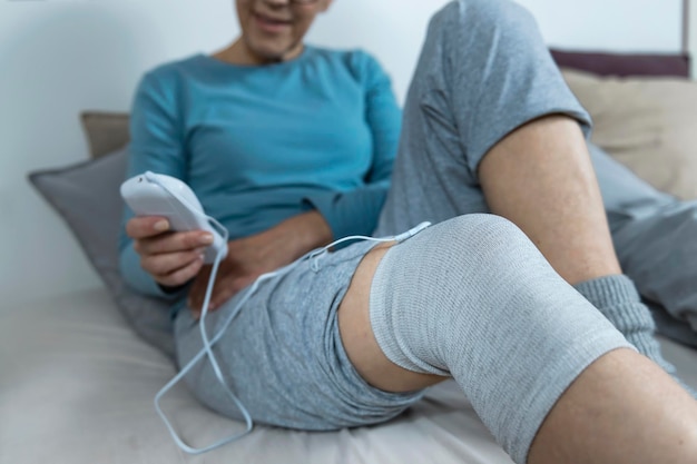 Przezskórna elektryczna stymulacja nerwów Starsza kobieta wykonująca fizjoterapię kolana za pomocą przewodzącej skarpety z elektrodą TENS