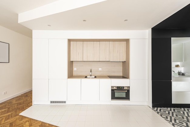 Przód ładnej, współczesnej otwartej kuchni z wbudowanymi szafkami bez uchwytów i mieszanymi kafelkami na podłodze