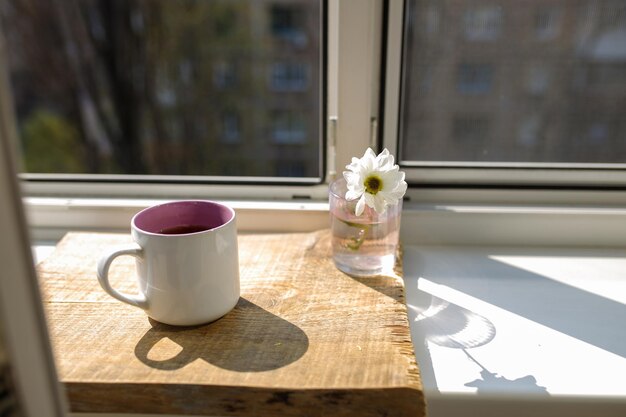 Przy oknie stoi filiżanka herbaty na drewnianej tacy