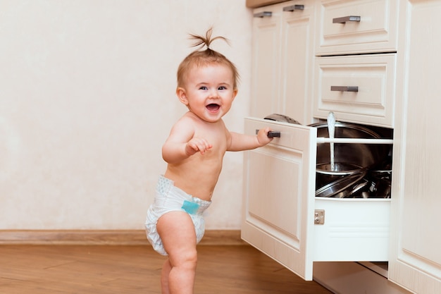 Przy otwartej szafce w kuchni stoi szczęśliwe dziecko. dzieciak w białej kuchni. dziecko uśmiecha się w białej kuchni.