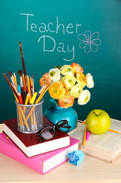 Zdjęcie przybory szkolne i kwiaty na tle tablicy z napisem dzień nauczyciela
