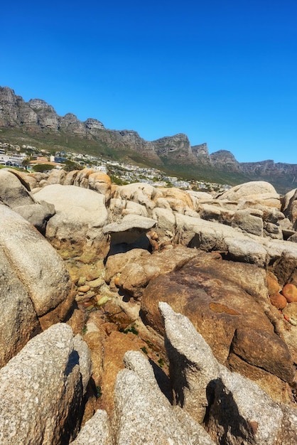 Przybrzeżne skały z widokiem na góry i miasto na tle błękitnego nieba z kopią przestrzeni Jasny letni krajobraz dużych kamieni natury z szorstkimi szczegółami tekstury w pobliżu luksusowych domów w Kapsztadzie