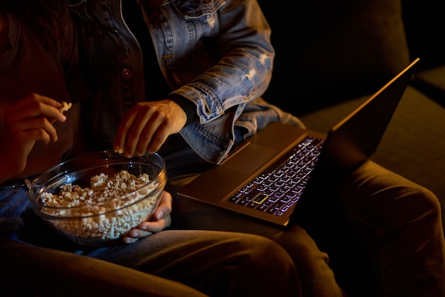 Przycięta para ogląda film na laptopie, jedząc popcorn w nocy przytulny dom w nocy, wolny czas razem, zrelaksowany mężczyzna i kobieta odpoczywają