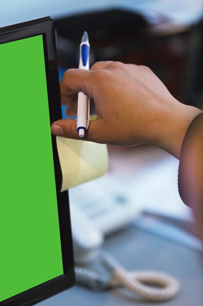 Zdjęcie przycięta ręka biznesmena przyklejającego notatkę na monitorze komputera w biurze