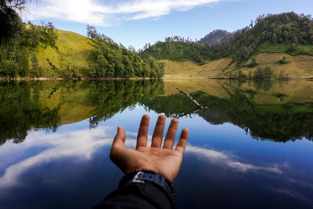 Zdjęcie przycięta ręka człowieka gestującego nad jeziorem przeciwko górom