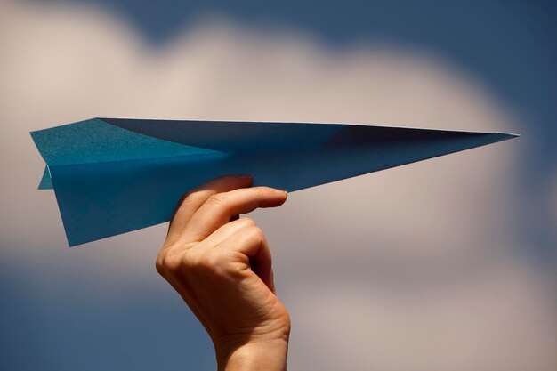 Przycięta ręka kobiety trzymającej papierowy samolot przeciwko niebu