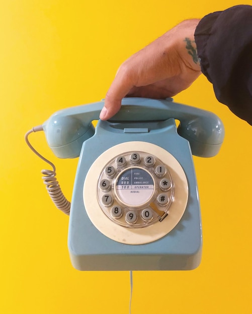 Przycięta ręka kobiety trzymającej telefon na żółtym tle