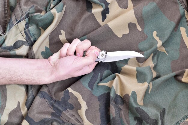 Zdjęcie przycięta ręka osoby trzymającej nóż nad odzieżą kamuflażową