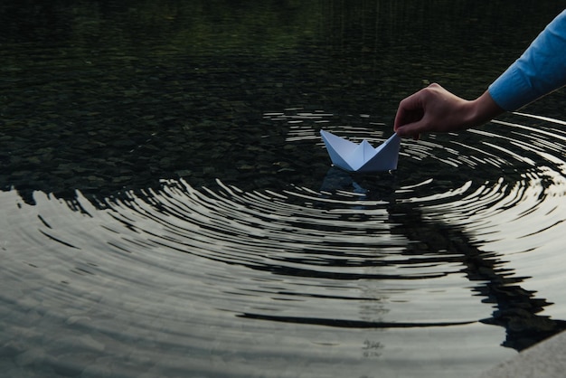 Zdjęcie przycięta ręka osoby trzymającej papierową łódź na jeziorze