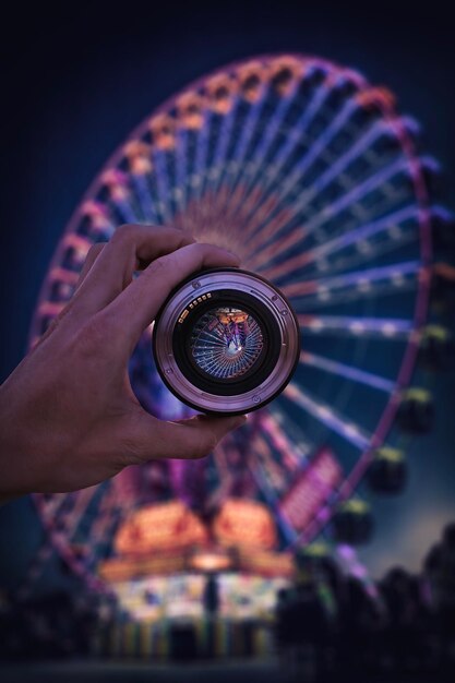Zdjęcie przycięta ręka trzymająca kamerę przed oświetlonym wielkim kołem w nocy
