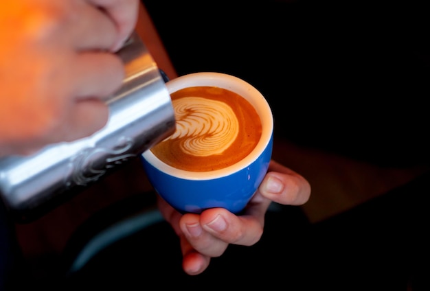 Przycięte ręce baristy nalewające mleko do filiżanki kawy w kawiarni