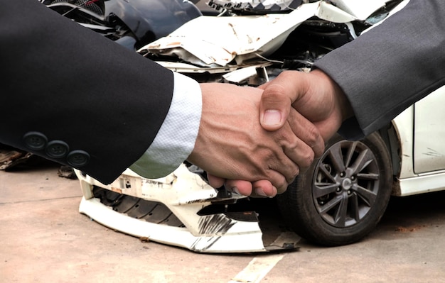 Zdjęcie przycięte ręce biznesmenów uściskających ręce przeciwko uszkodzonemu samochodowi