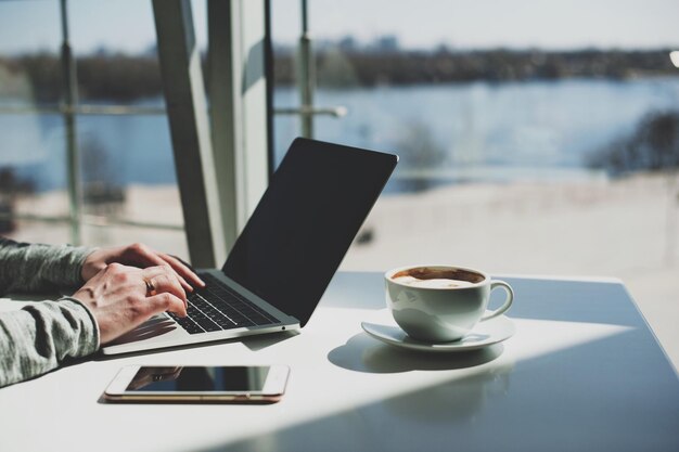 Zdjęcie przycięte ręce pracujące na laptopie przy kawie.