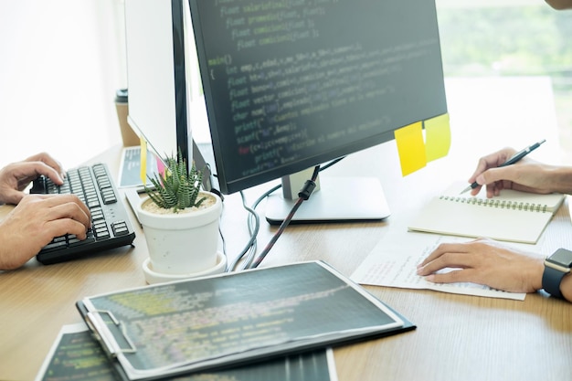 Przycięte ręce programistów kodujących na komputerach w biurze.