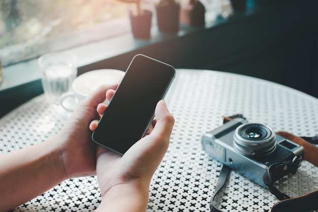 Przycięte ręce trzymające telefon komórkowy przy stole w kawiarni