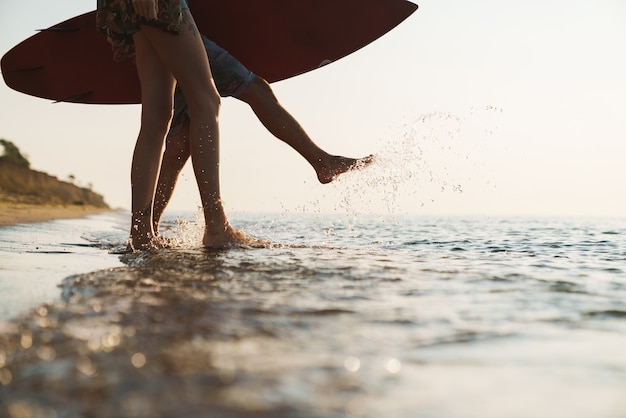 Przycięte Zdjęcie Kaukaskiej Pary Trzymającej Deskę Surfingową Podczas Spaceru Po Słonecznej Plaży