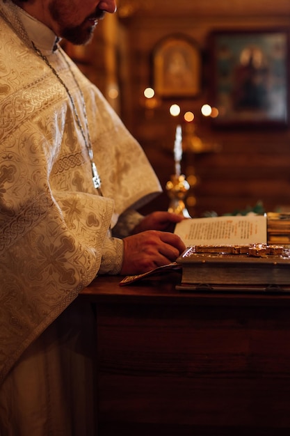 Zdjęcie przycięte zdjęcie księdza nosi uroczystą sutannę stojącą na mównicy z książkami czytającymi modlitewnik w cerkwi