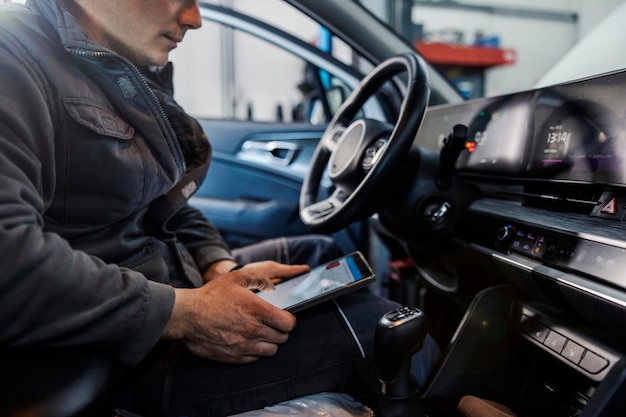 Przycięte zdjęcie mechanika siedzącego w samochodzie z tabletem w dłoniach i wykonującego przegląd techniczny