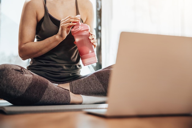 Przycięte zdjęcie młodej kobiety za pomocą laptopa podczas treningu fitness w domu.