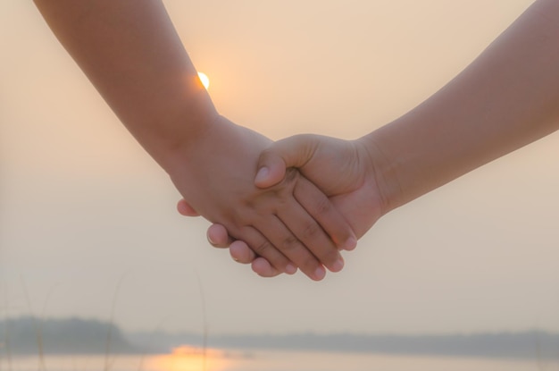 Przycięte zdjęcie przyjaciół trzymających się za ręce na niebie podczas zachodu słońca