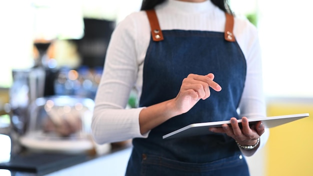 Przycięte zdjęcie właściciela małej firmy kobieta za pomocą cyfrowego tabletu i stojąc przed barem w kawiarni.