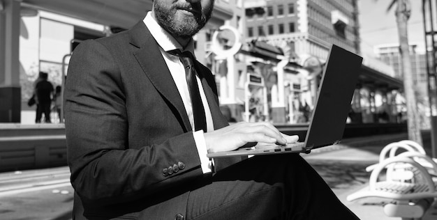 Zdjęcie przycięty mężczyzna biznesmen siedzi na ławce w mieście na świeżym powietrzu, pracując online na blogu biznesowym na laptopie