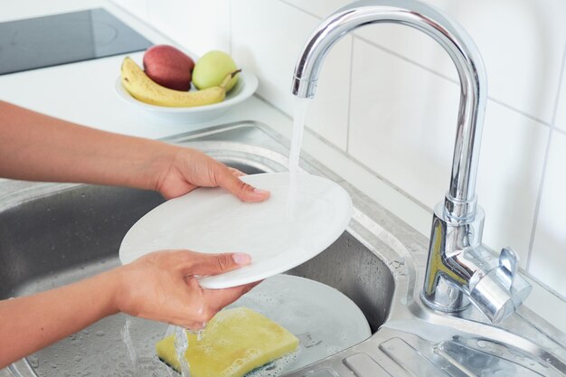 Przycięty obraz atrakcyjnej młodej kobiety myje naczynia podczas sprzątania w domu