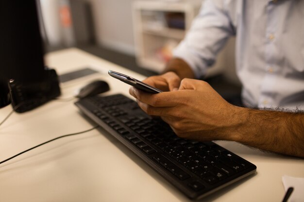 Przycięty obraz biznesmena przy użyciu telefonu komórkowego, siedząc przy biurku