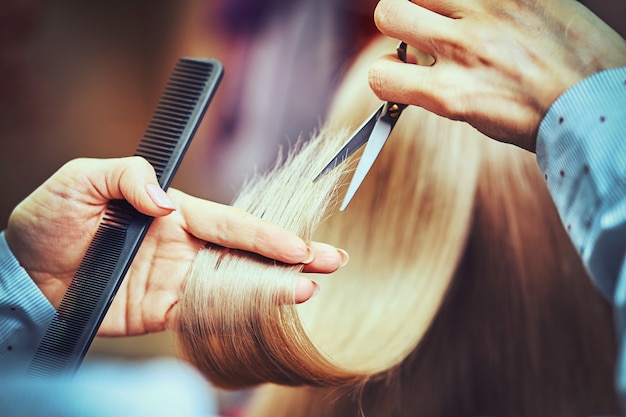 Przycięty obraz fryzjera przycinającego końce blond włosów