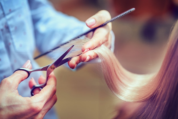 Przycięty obraz fryzjera przycinającego końce blond włosów