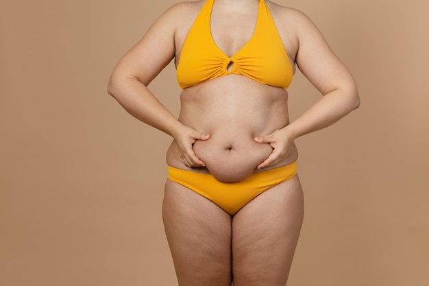 Przycięty obraz grubej kobiety z nadwagą i otyłością z nadmiarem tkanki tłuszczowej żółty strój kąpielowy Samoakceptacja ciało pozytywne