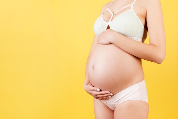 Przycięty obraz kobiety w ciąży przytulającej brzuch Matka ma na sobie kolorową bieliznę na żółtym tle Przyszły rodzic spodziewa się dziecka