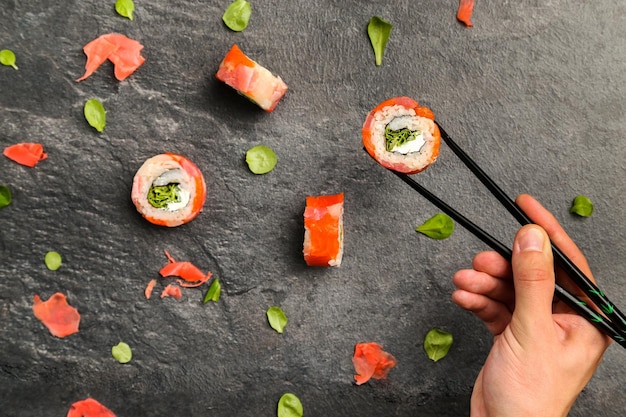 Przycięty obraz ręki trzymającej sushi z pałeczkami na kamiennej tacce