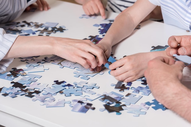 Przycięty obraz Rodzina bawiąca się puzzlami na stole w domu razem