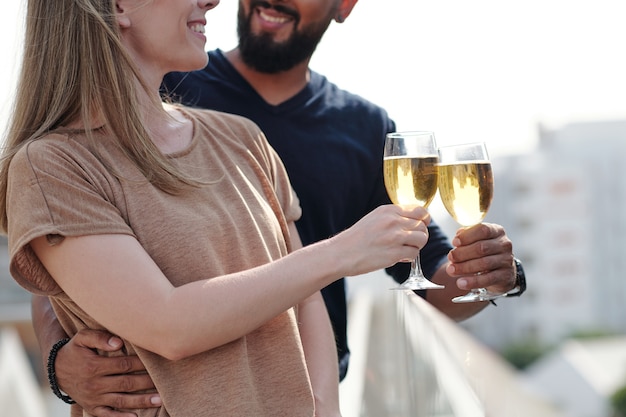 Przycięty obraz uśmiechniętej przytulającej się młodej pary cieszącej się piciem szampana na dachu