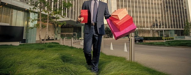 Przycięty przedsiębiorca w garniturze trzymający torbę na zakupy i pudełko na prezenty poza biurem nagrody