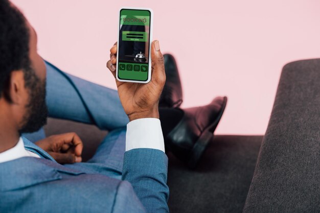 Zdjęcie przycięty widok afrykańskiego biznesmena pokazującego smartfona z aplikacją do rezerwacji odizolowaną na różowo