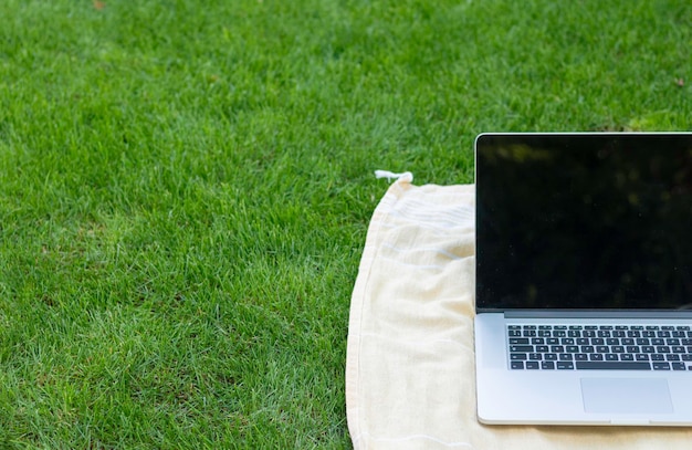 Przycięty widok laptopa opartego na ręczniku w podłodze ogrodu z zieloną świeżą trawą