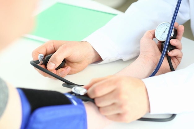Przycięty widok męskiego lekarza sprawdzającego ciśnienie krwi pacjenta przy stole